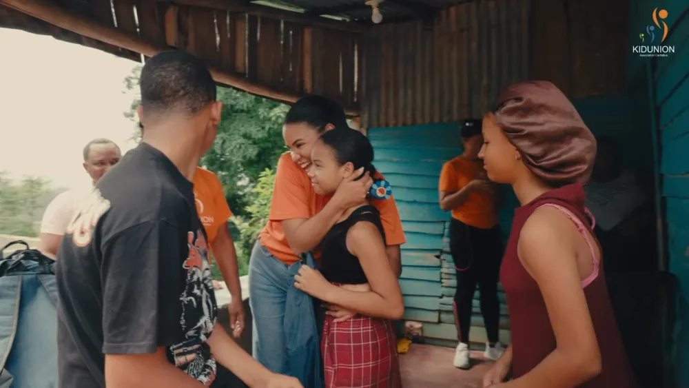 Voluntaria de KIDUNION abraza a una niña durante la entrega de mochilas en Bonao